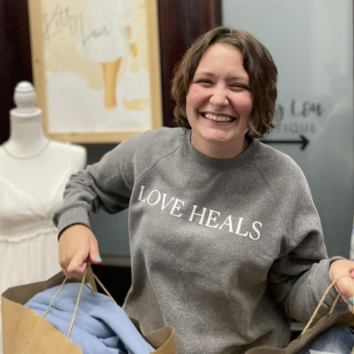 Cassie Wolfe, wearing a sweatshirt that says, “Love Heals,” holds up bags from a successful shopping trip.